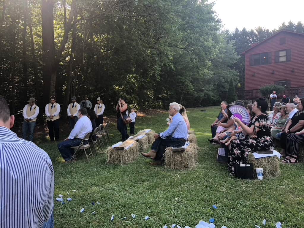 Outdoor gathering at Tanglewood Cabin with guests seated on hay bales in a lush, wooded setting.